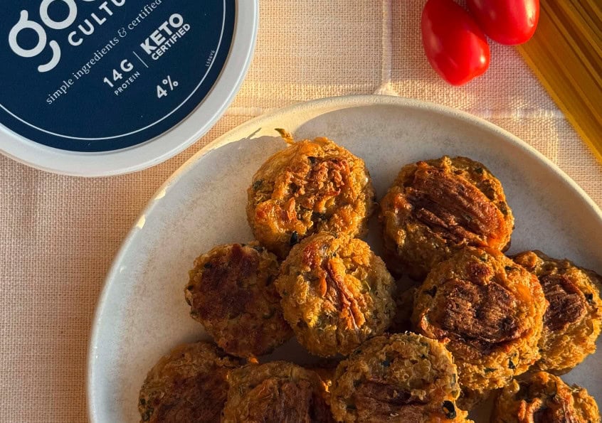 Golden-brown veggie meatballs made with Good Culture cottage cheese, served on a white plate beside fresh cherry tomatoes and a container of Good Culture 4% cottage cheese.