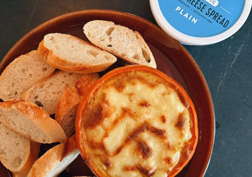 Warm roasted pumpkin and sage dip baked with melted cheese, served in a dish surrounded by toasted baguette slices and a container of Good Culture cheese spread.